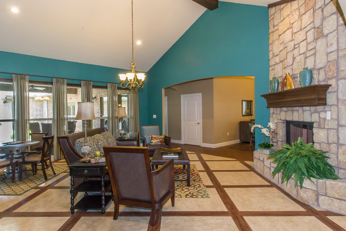 A spacious living room featuring a vaulted ceiling, blue accent wall, and a fireplace, with elegant furniture and a chandelier.