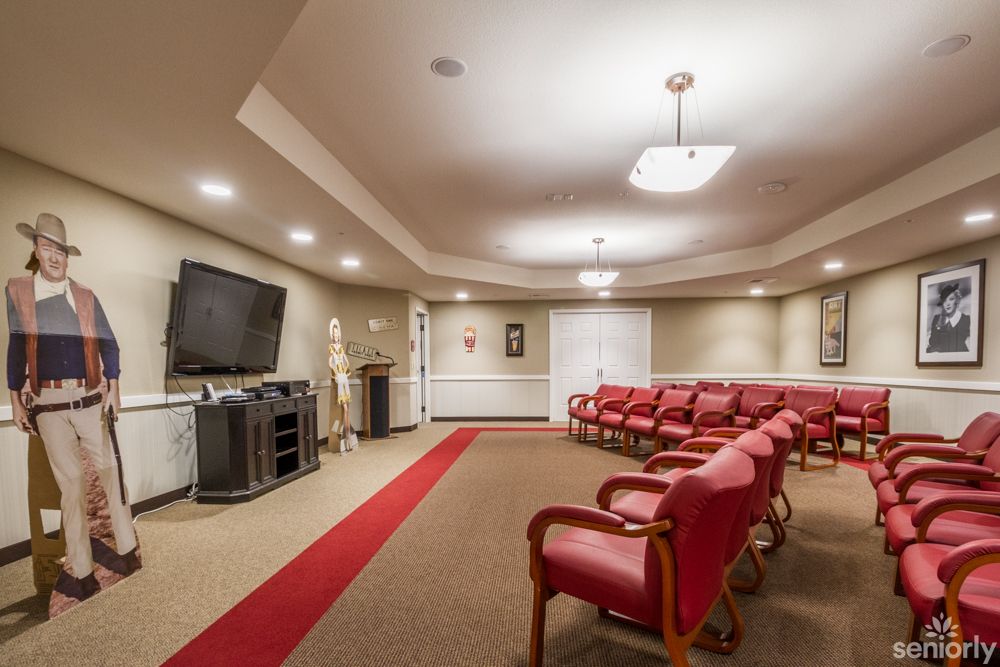 A conference room with red chairs arranged around the perimeter, a large television, and a carpeted floor.
