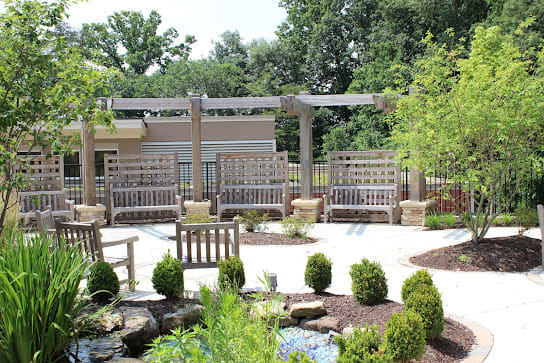 A beautifully landscaped garden with benches and a pergola, surrounded by lush greenery.