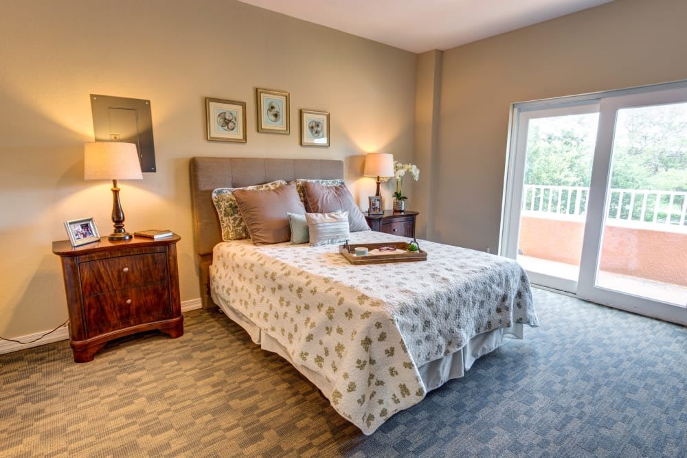 A cozy bedroom with elegant decor featuring a comfortable bed, nightstands with lamps, and a large window allowing natural light.
