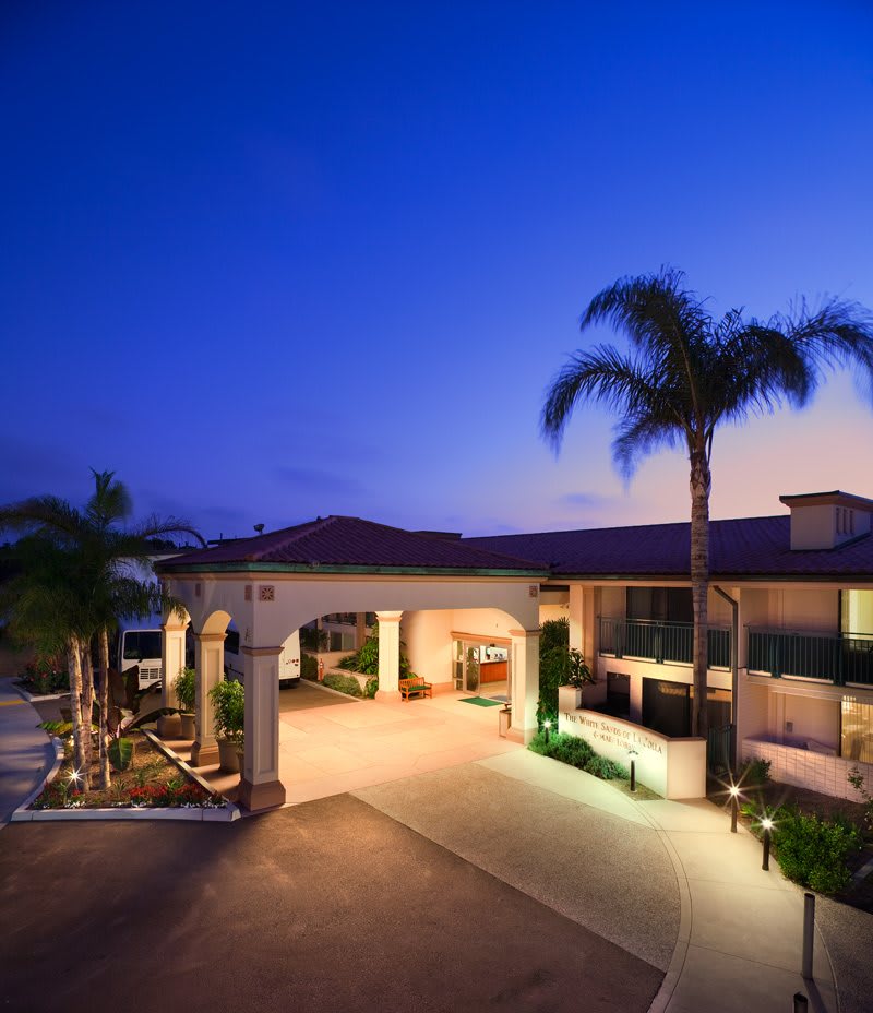 A modern building entrance illuminated at dusk, framed by palm trees.