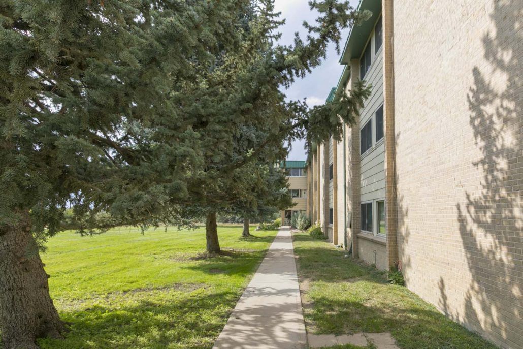 A sidewalk lined with trees adjacent to an apartment building.