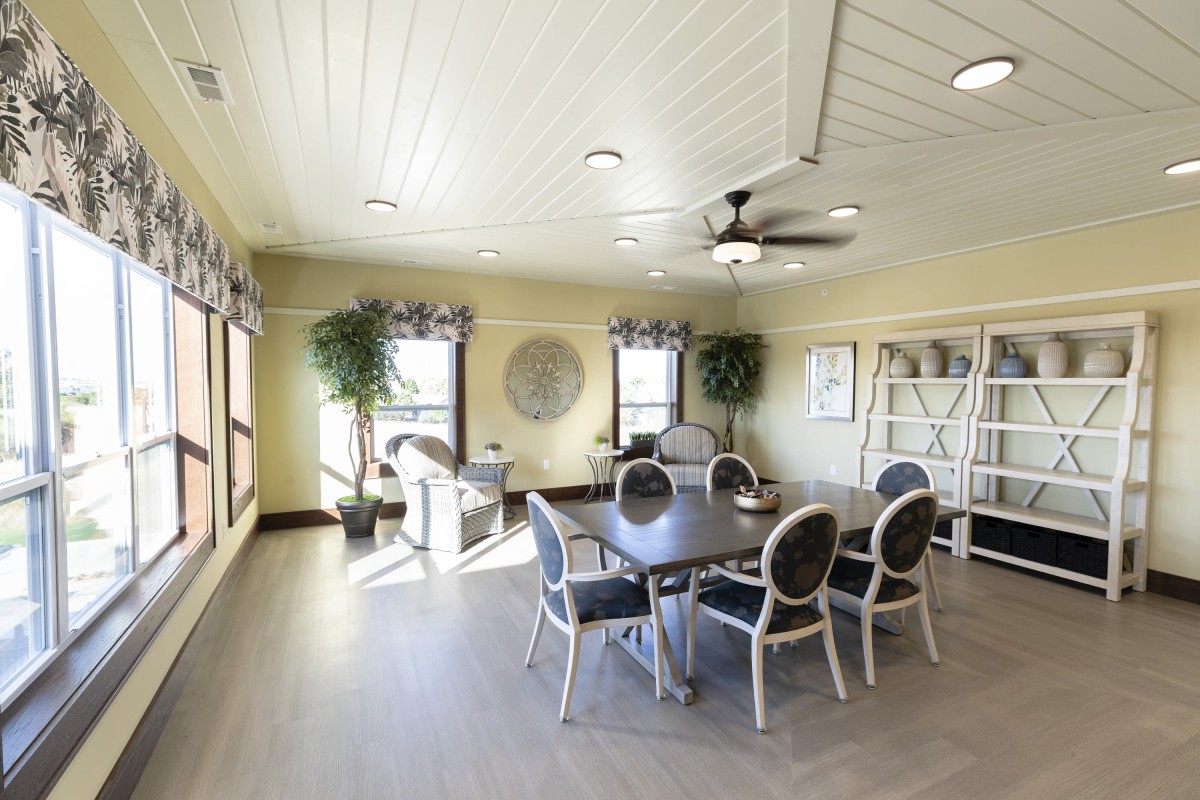A bright dining room with a round table, six chairs, large windows, and decorative plants.