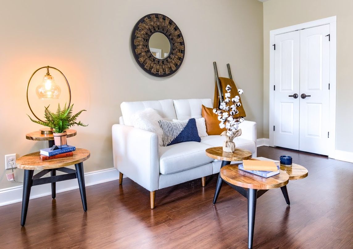 A modern living room with a white sofa, wooden coffee tables, a decorative mirror, and a potted plant.