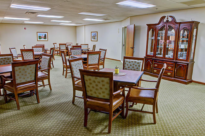 A spacious dining room with multiple tables and chairs, decorated with a wooden cabinet.