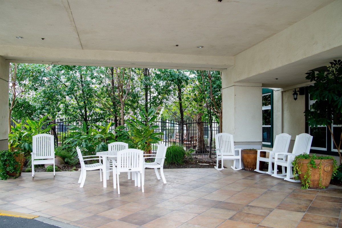 A cozy outdoor patio with white furniture surrounded by lush greenery.