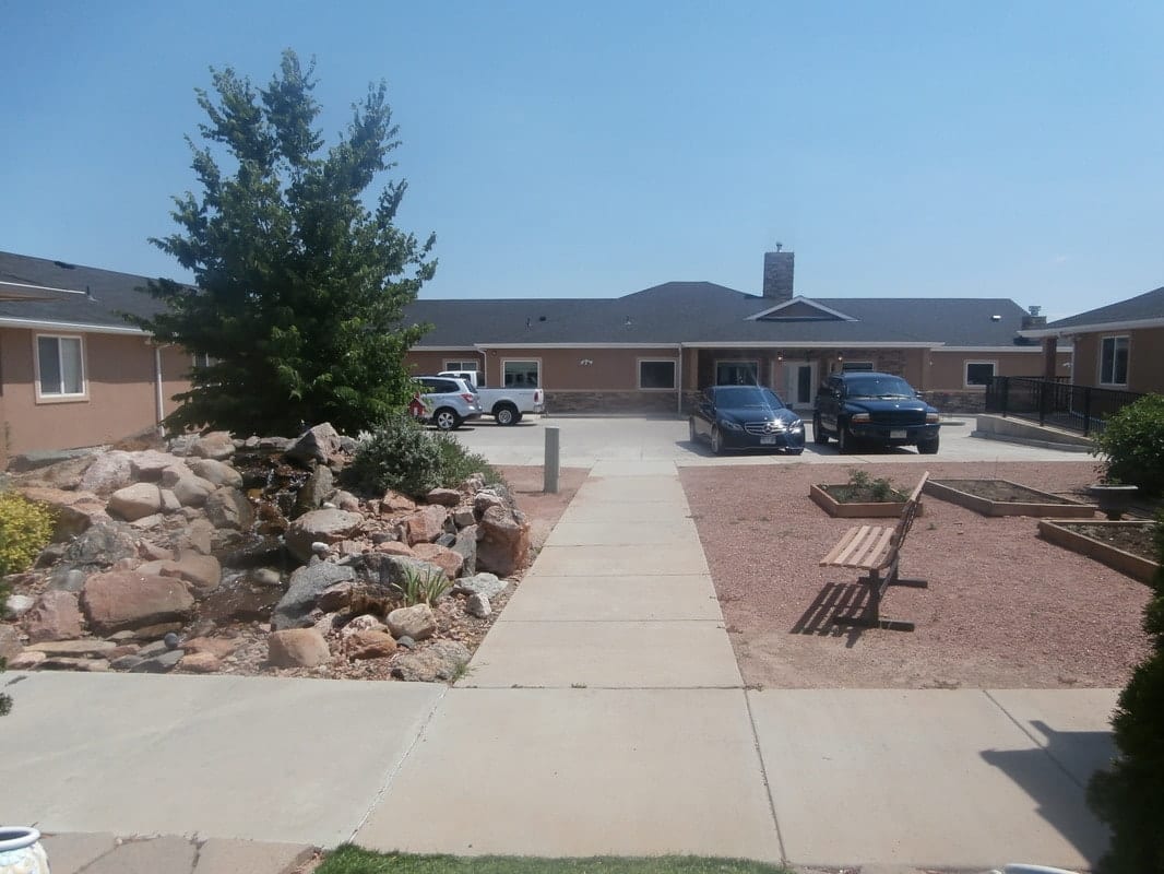 A building with a parking lot and landscaped walkway featuring benches and rocks.