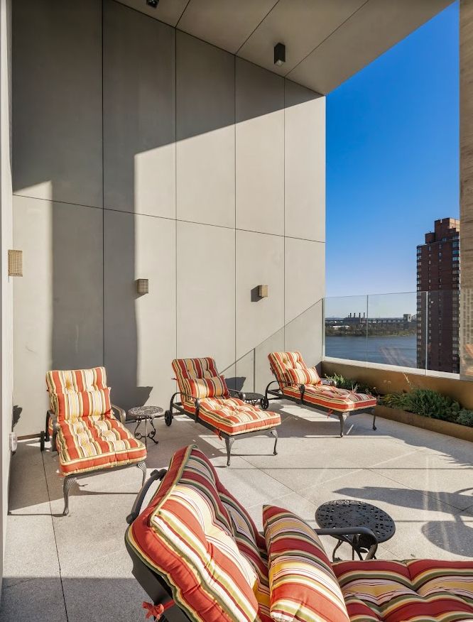 A modern balcony with comfortable lounge chairs offering a scenic city and river view on a sunny day.