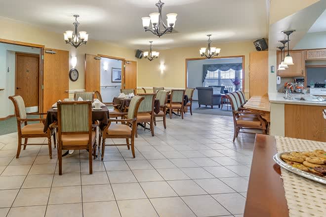 A well-lit dining room with multiple tables and chairs, featuring chandeliers and a tiled floor.