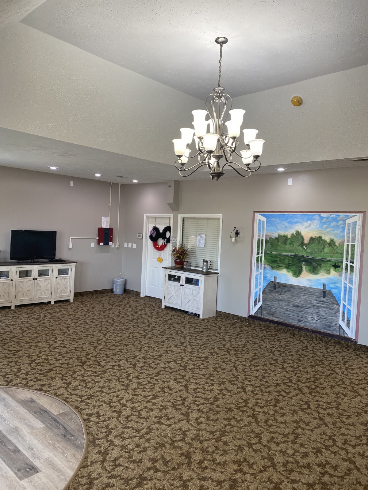 A cozy living room with a chandelier and a decorative wall painting.