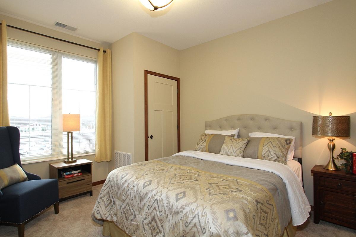 Cozy bedroom with a comfortable bed, bedside lamp, and natural light from the window.