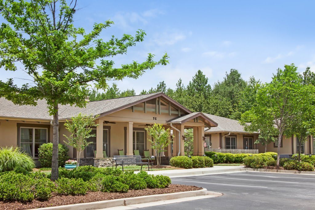 A single-story building surrounded by lush greenery and trees with a parking area in front.