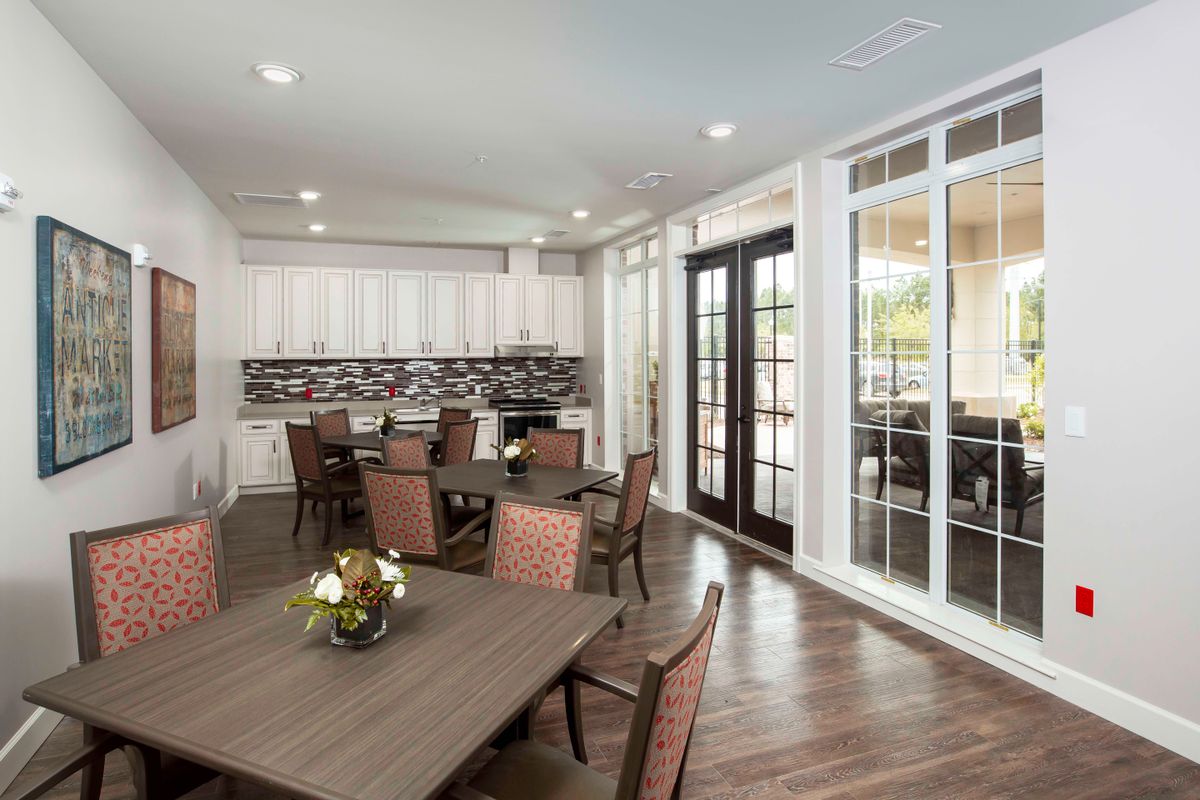 A modern dining room with wood flooring, tables and chairs, and decorative flowers, featuring large windows that offer ample natural light.