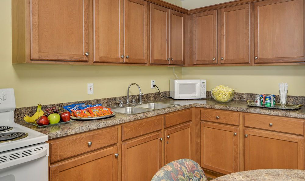 A kitchen with wooden cabinets, granite countertops, a microwave, and snacks on the counter.
