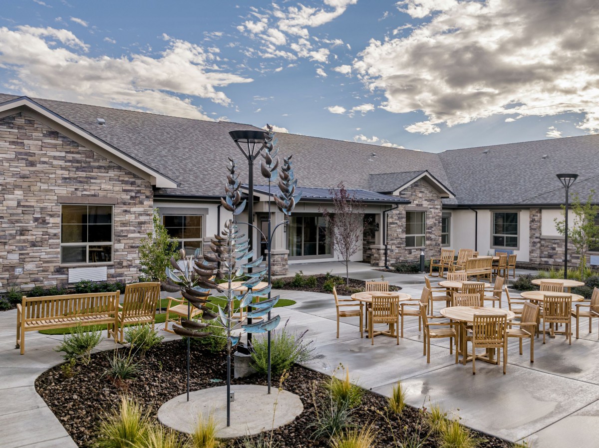 A serene courtyard featuring outdoor seating with wooden tables and chairs, surrounded by stone-walled buildings and landscaped greenery.