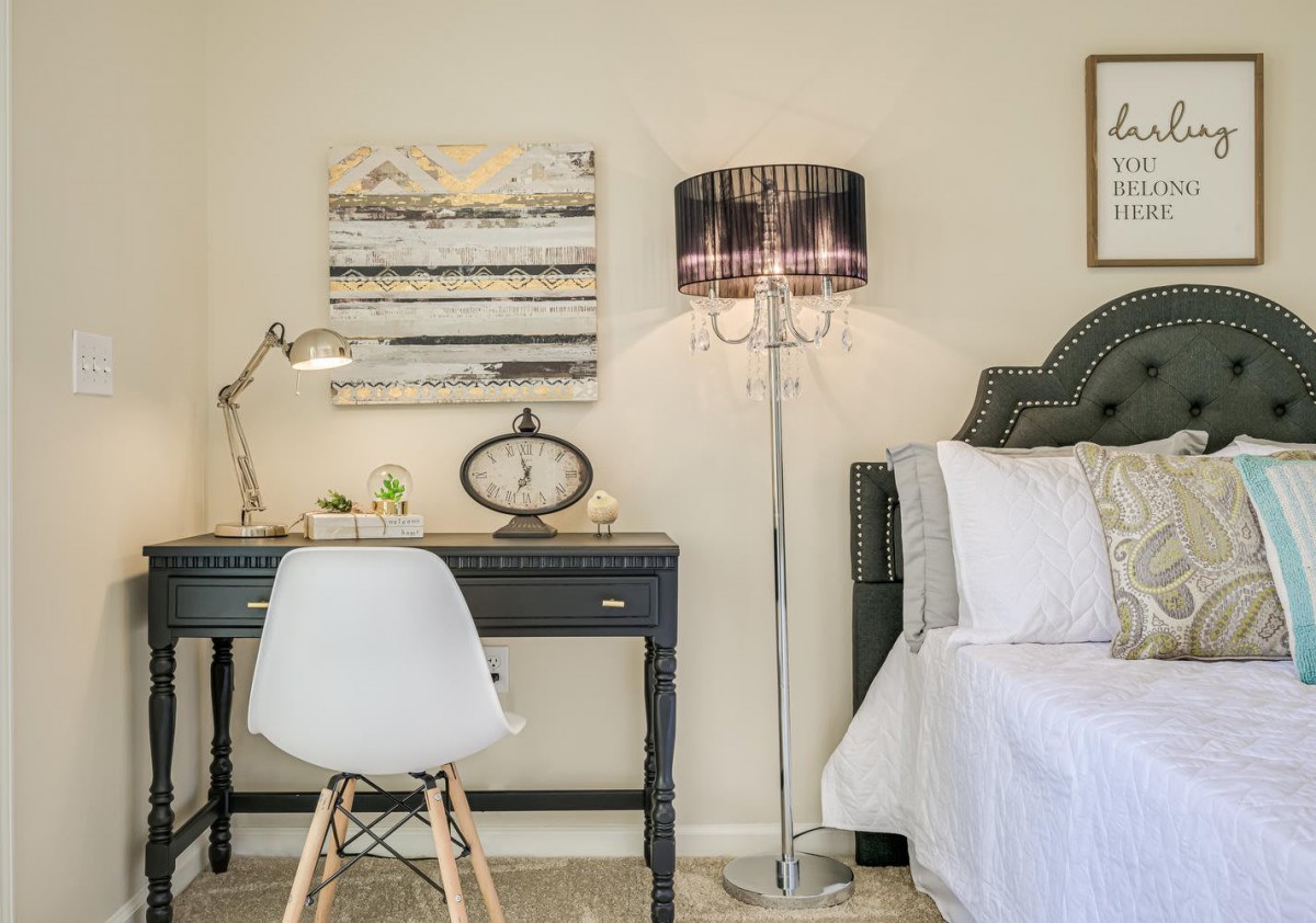 A cozy bedroom corner with a desk, chair, and floor lamp next to a bed.