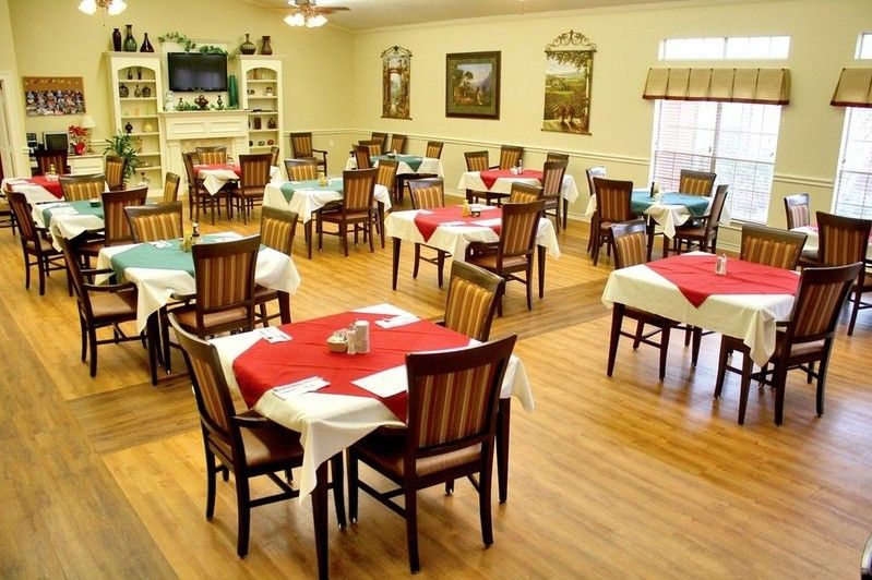 A well-arranged dining area with multiple tables and chairs, featuring colorful tablecloths and a wooden floor.
