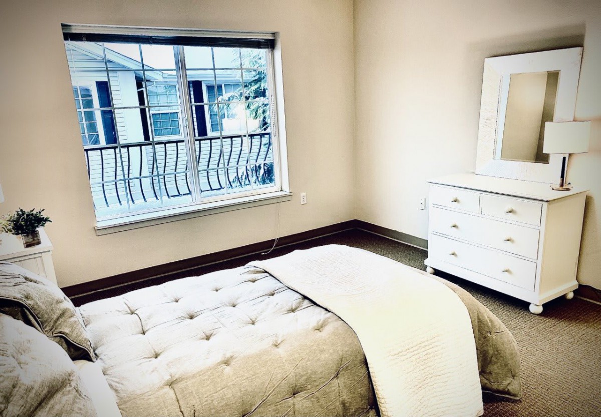 A minimalist bedroom with a bed and dresser near a large window.