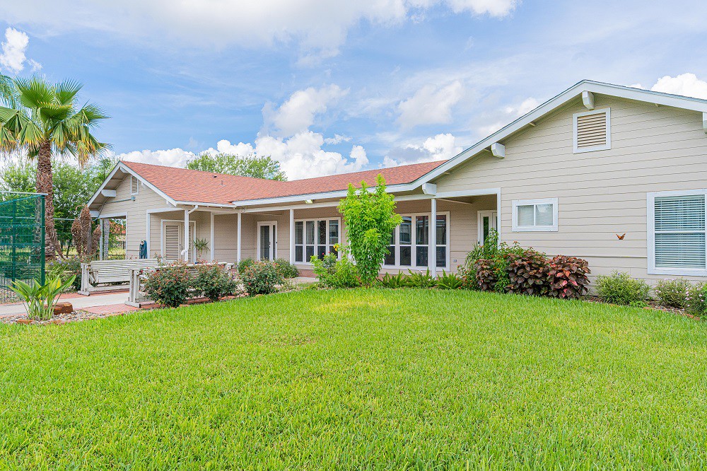 A single-story house with a red roof and well-maintained lawn under a blue sky.