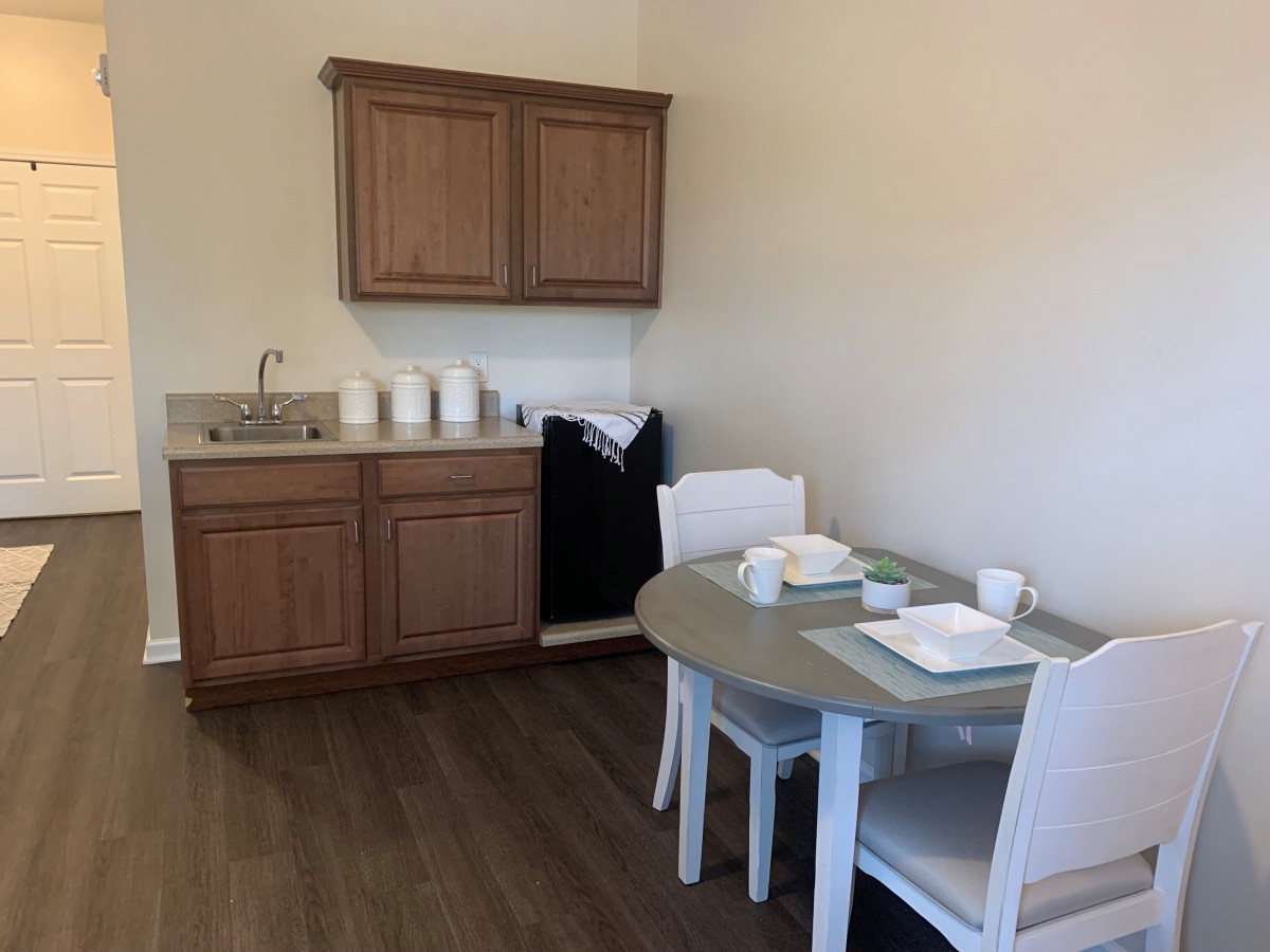 A compact kitchenette with wooden cabinets, a small dining table, and chairs.