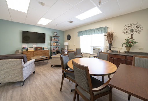 A cozy and well-lit meeting room featuring comfortable seating, tables for discussion, and a large television.