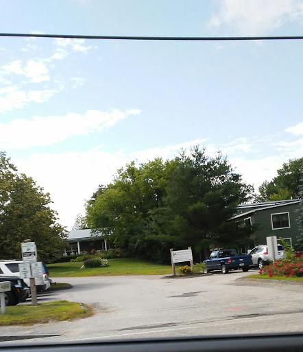 A view of a parking area surrounded by trees and buildings under a partly cloudy sky.