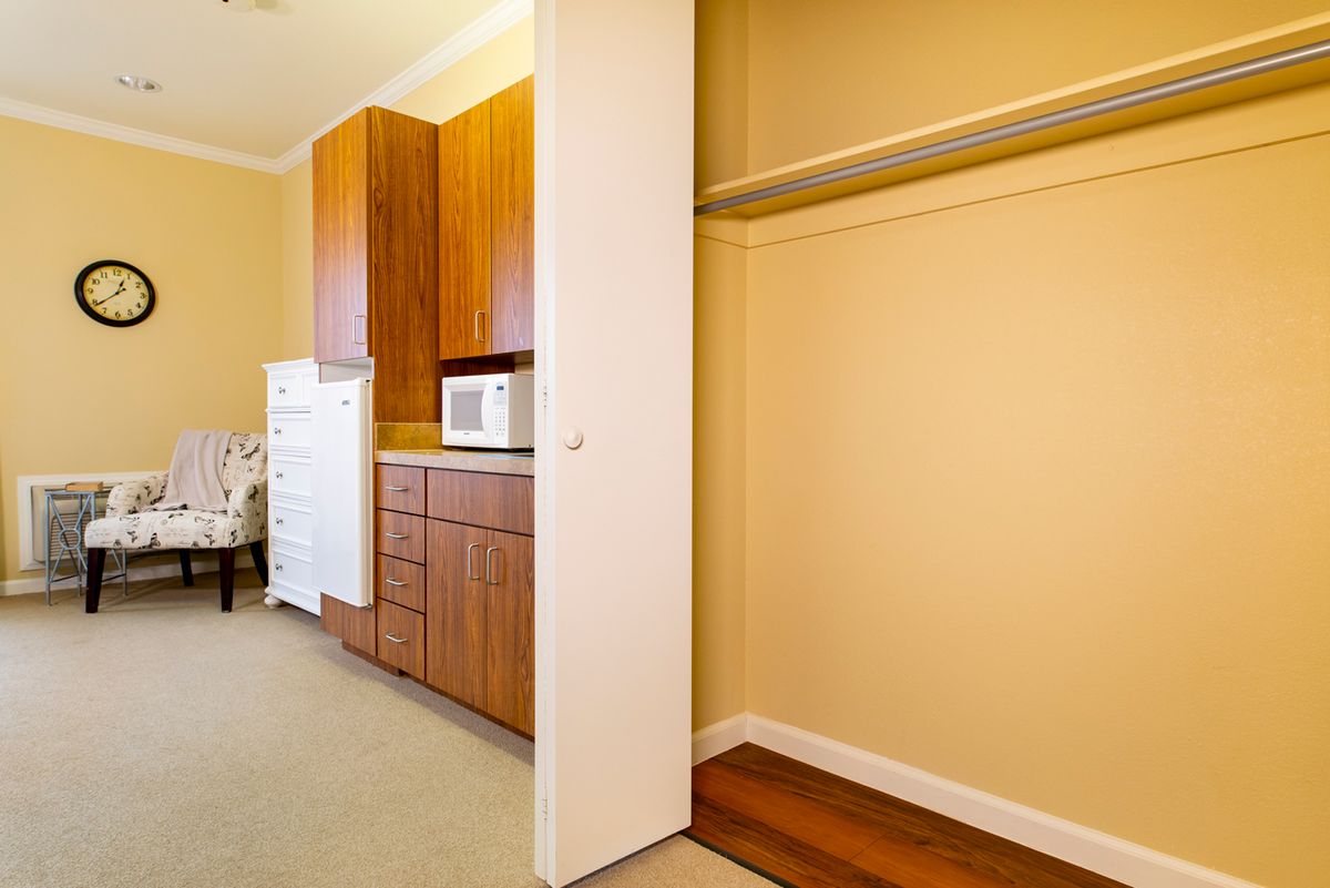 A kitchen area with wooden cabinets and a microwave next to an open closet.