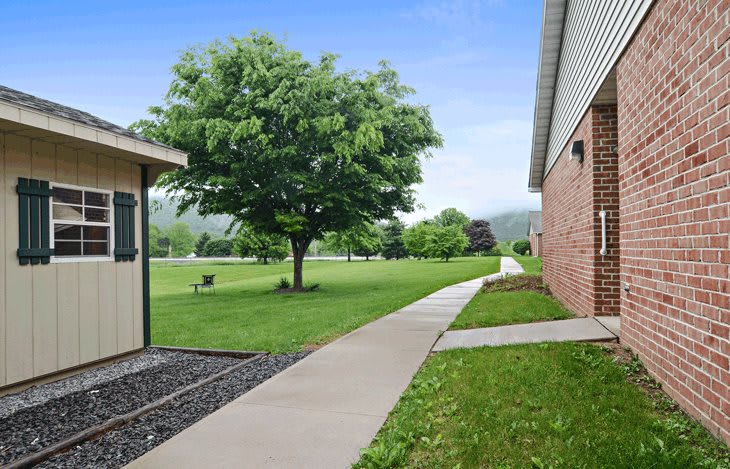 A scenic outdoor view featuring a walkway between buildings, with lush green grass and trees.