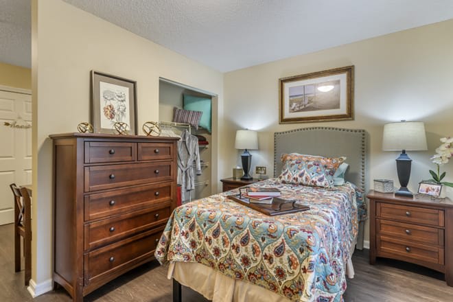 A cozy bedroom with a neatly made bed, wooden dresser, and decorative artworks on the walls.