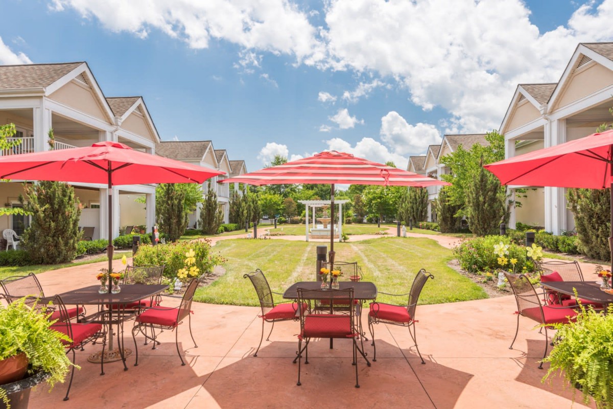 A sunny residential courtyard with patio tables, chairs, and umbrellas.