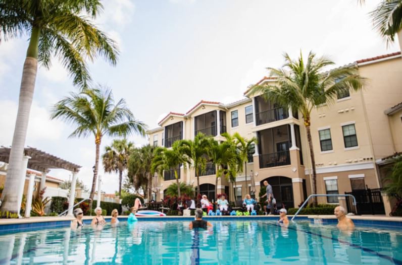 A lively apartment complex pool area with people enjoying the sun and water.