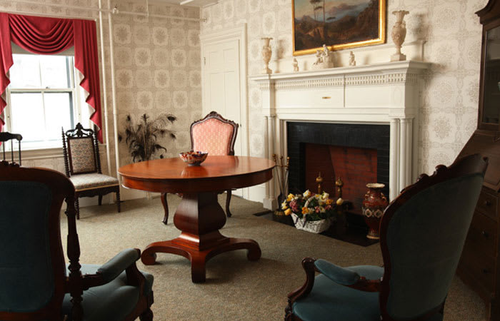 A vintage living room with antique furniture, featuring a round table, armchairs, and a fireplace.