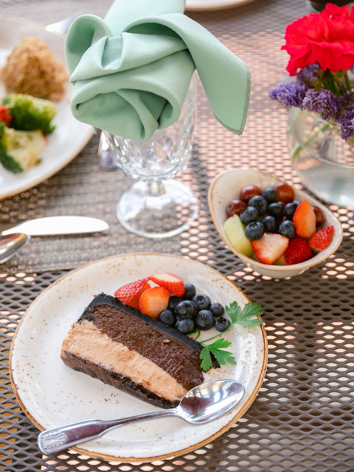 A slice of chocolate cake with fresh berries served alongside a bowl of mixed fruit on an elegantly set table.