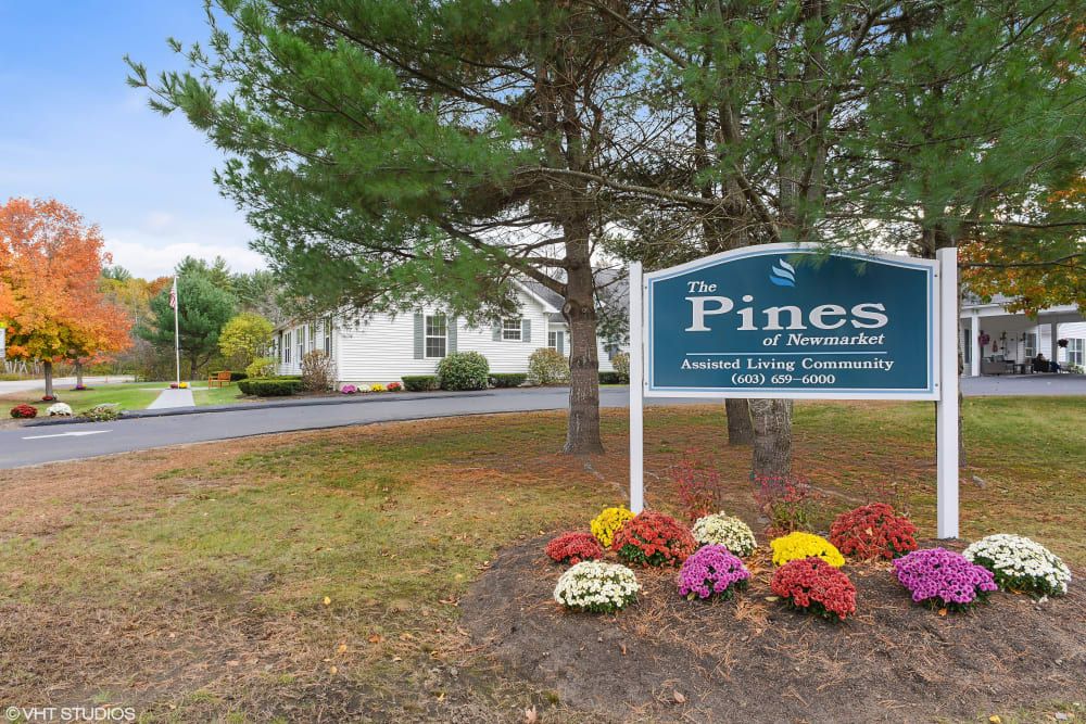 A landscaped entrance sign for 'The Pines' with colorful flowers and trees nearby.