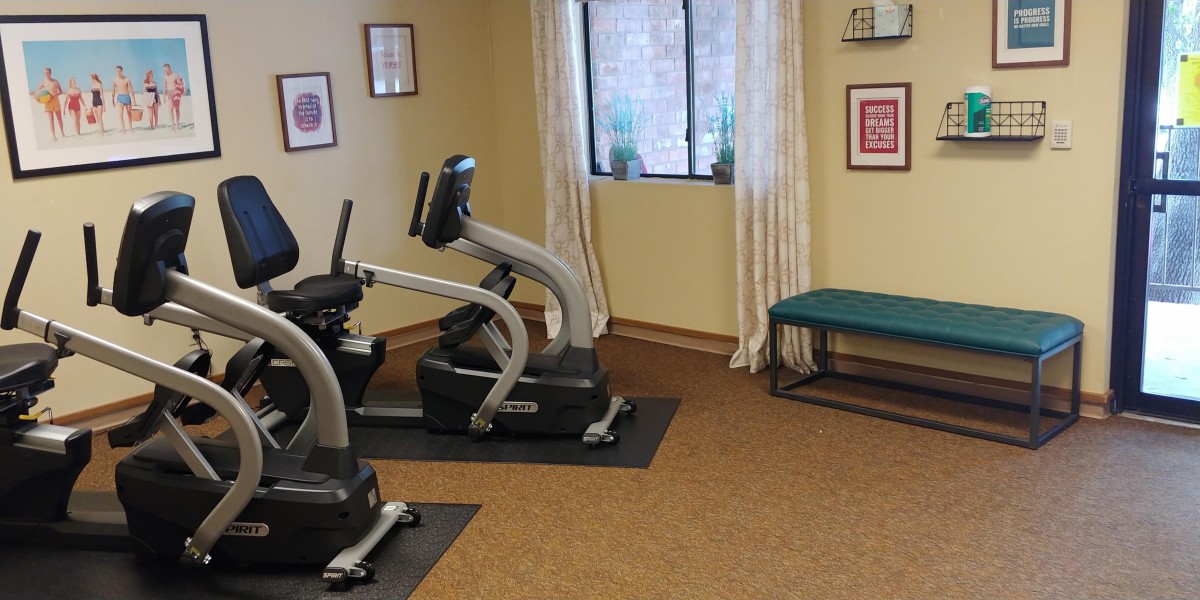 A small exercise room featuring stationary bikes and a bench, with wall art and a window providing natural light.
