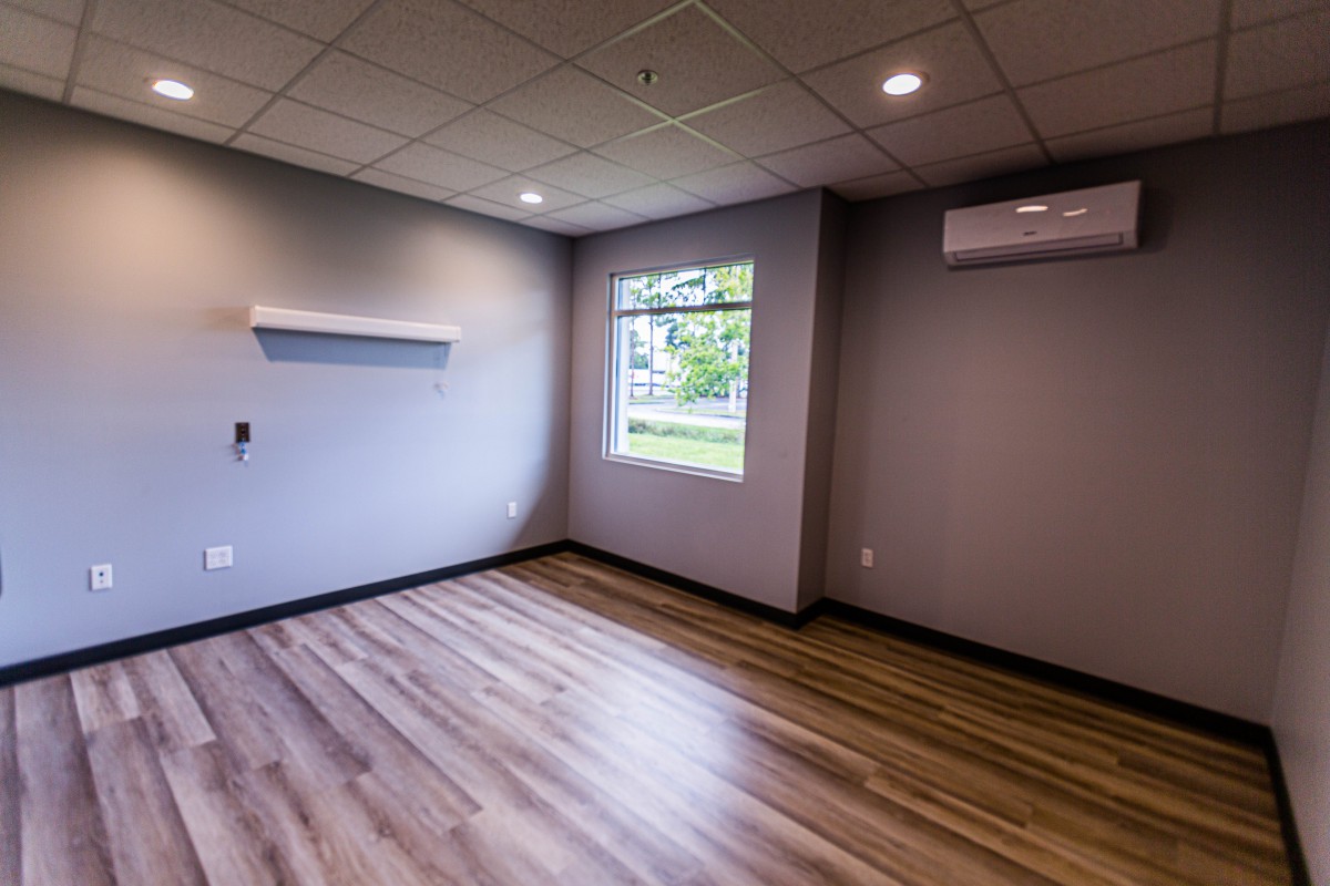 An empty room with hardwood flooring, ceiling lights, and an air conditioner.