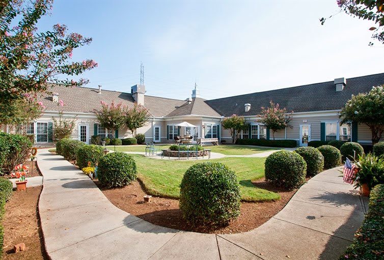 A well-maintained courtyard with trimmed bushes and a central fountain, surrounded by a large building.