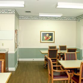 A neatly arranged dining room with tables and chairs, featuring artwork on the wall and overhead lighting.