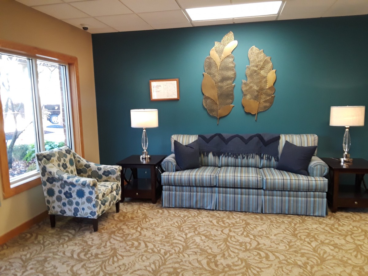A cozy living room with a blue plaid couch, decorative pillows, a patterned armchair, and metallic wall art.