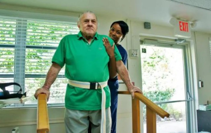An elderly man receiving assistance from a healthcare professional during physical therapy.