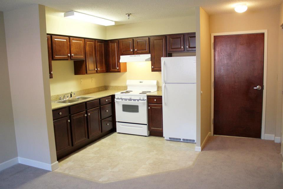 A compact kitchen with wooden cabinets, a stove, and a refrigerator in an apartment.