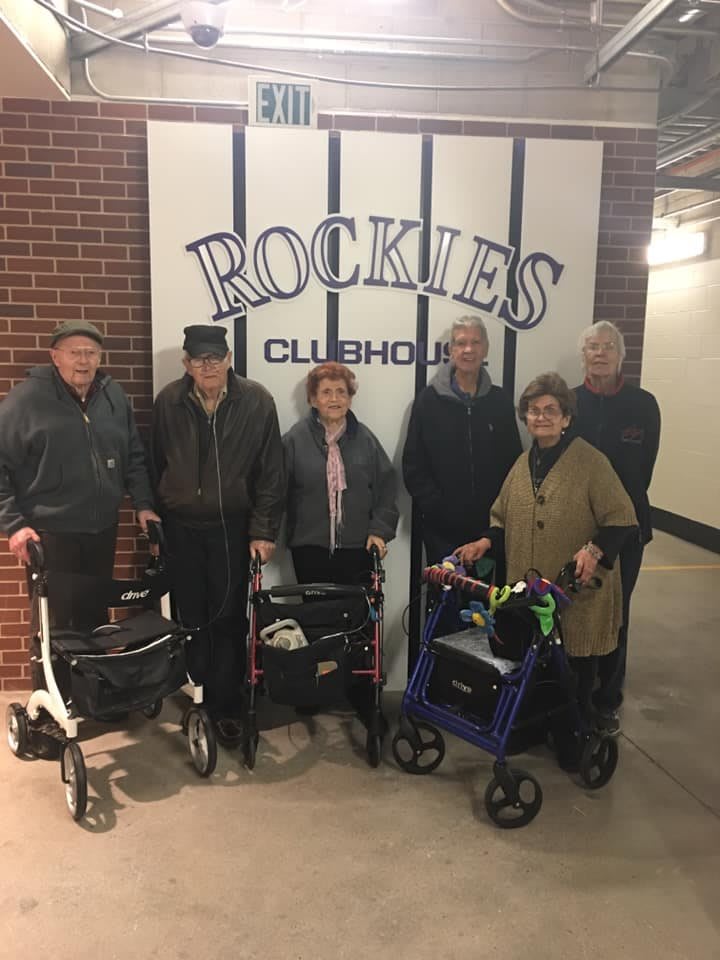 A group of seniors standing together with walkers in front of the Rockies clubhouse.