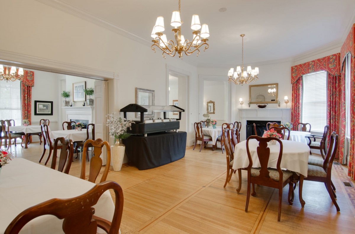 An elegant dining room with chandeliers, set tables, and wooden flooring.