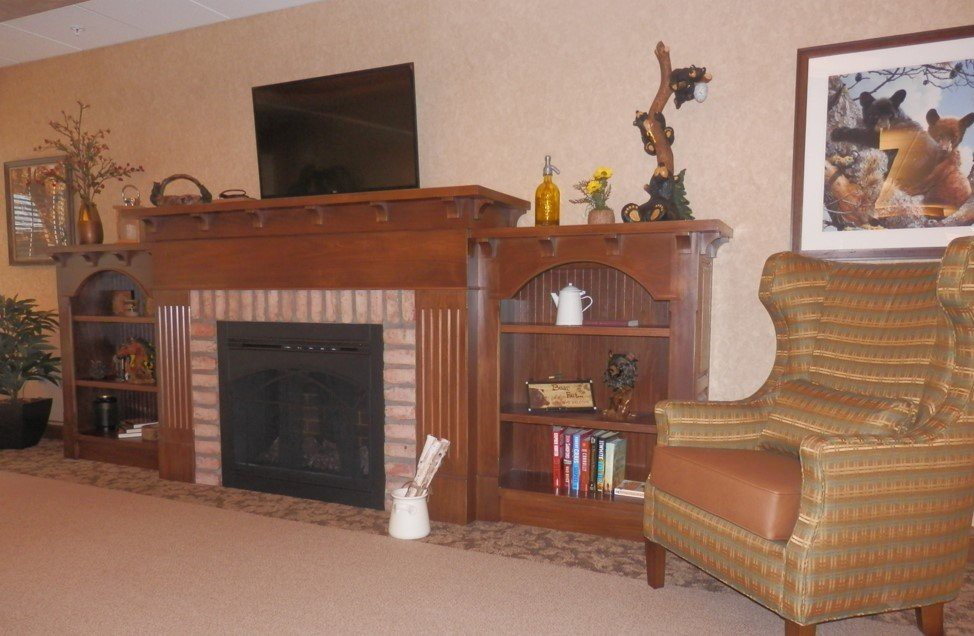 A cozy living room featuring a fireplace, bookshelf with decor, and an armchair.
