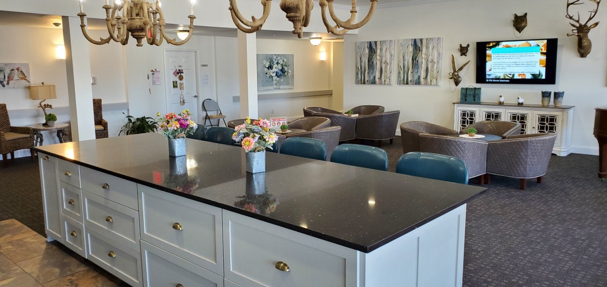 A modern kitchen with a dark countertop and floral decorations, overlooking a cozy living area.