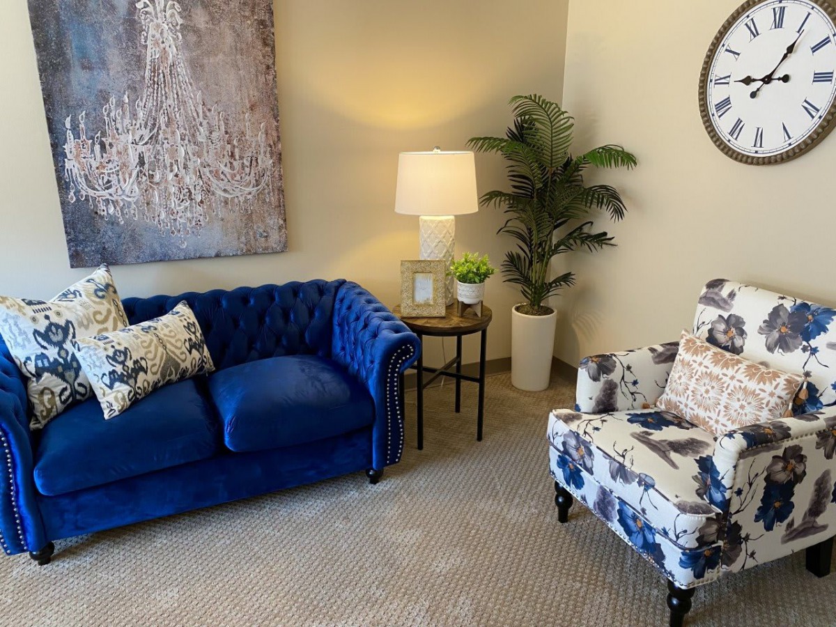 A cozy living room with a blue sofa, patterned armchair, and decorative elements.
