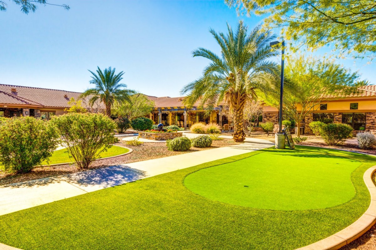 A beautifully landscaped garden featuring palm trees, a green lawn, and a pathway on a sunny day.