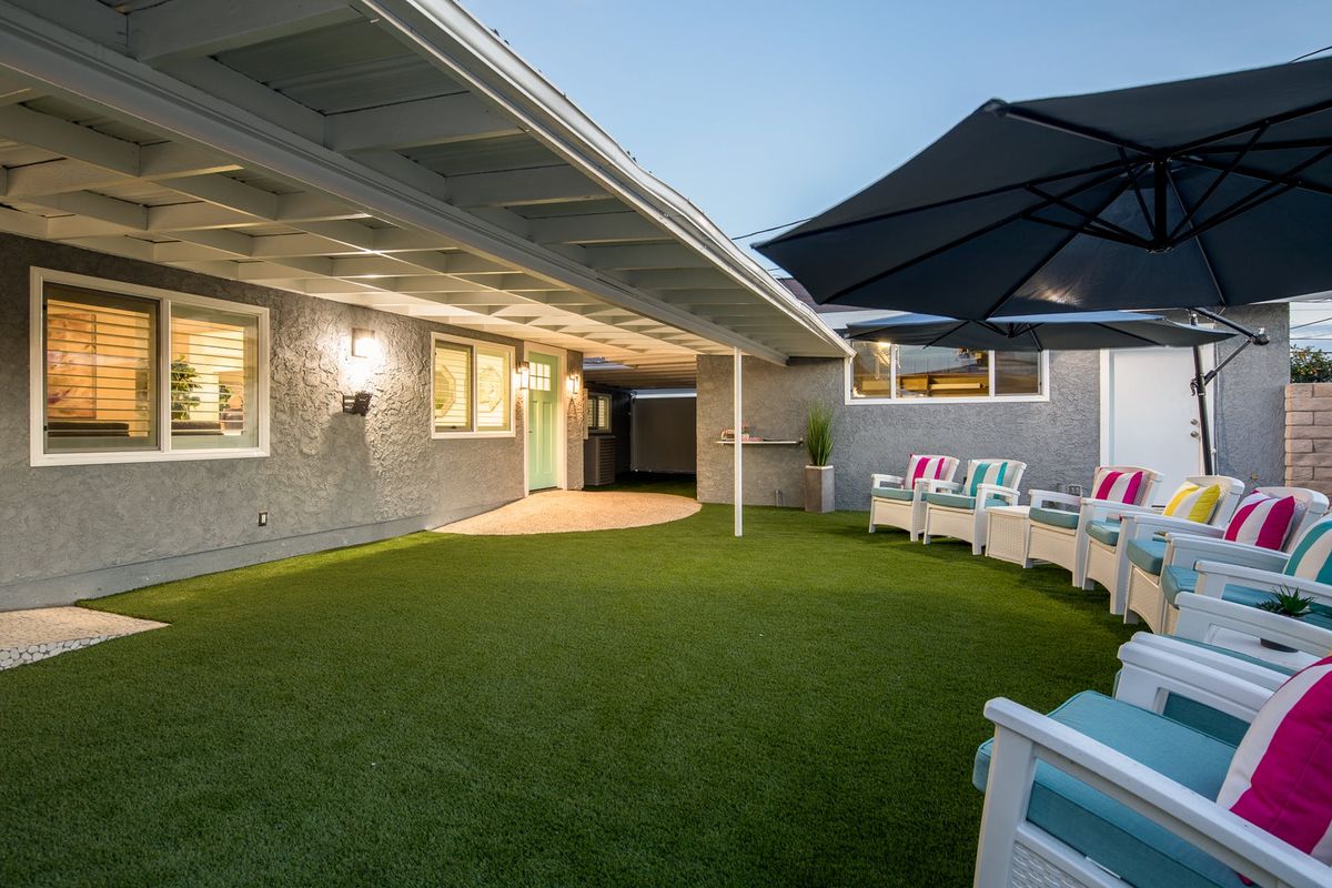 A cozy backyard patio with artificial grass, comfortable seating, and a large umbrella, perfect for evening relaxation.
