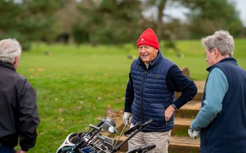 An elderly man enjoying a day on the golf course, wearing a bright red hat and a cozy vest.
