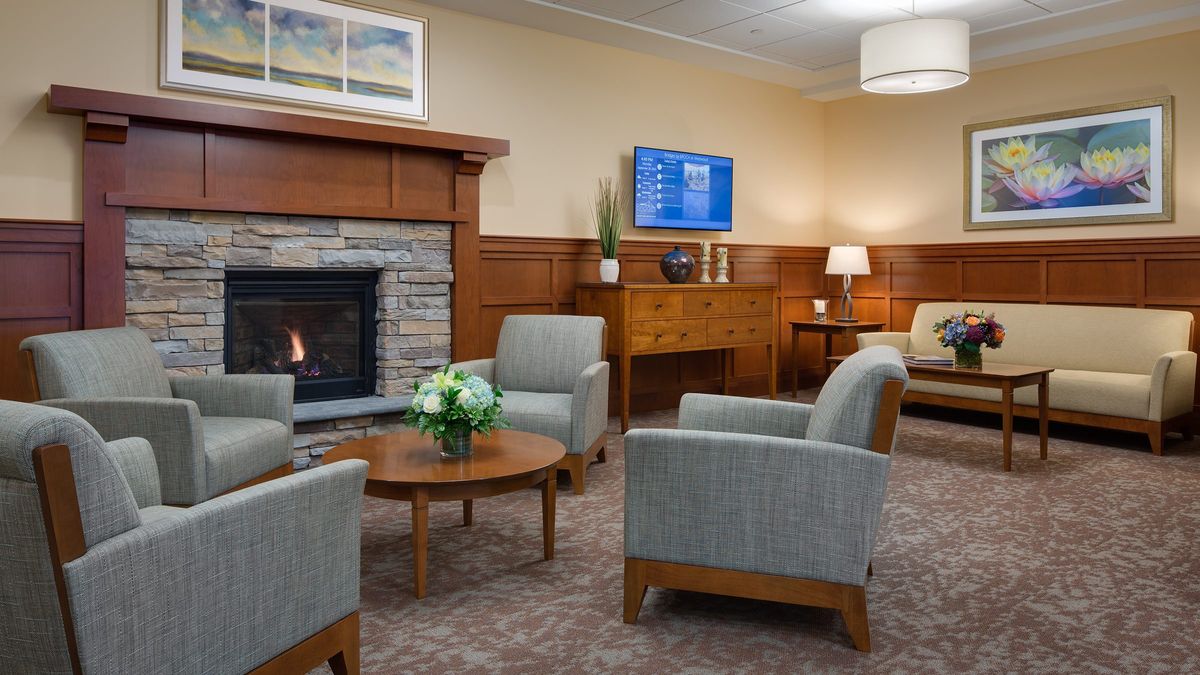 A cozy waiting room with comfortable chairs around a wooden coffee table, a warm fireplace, and tasteful decor.